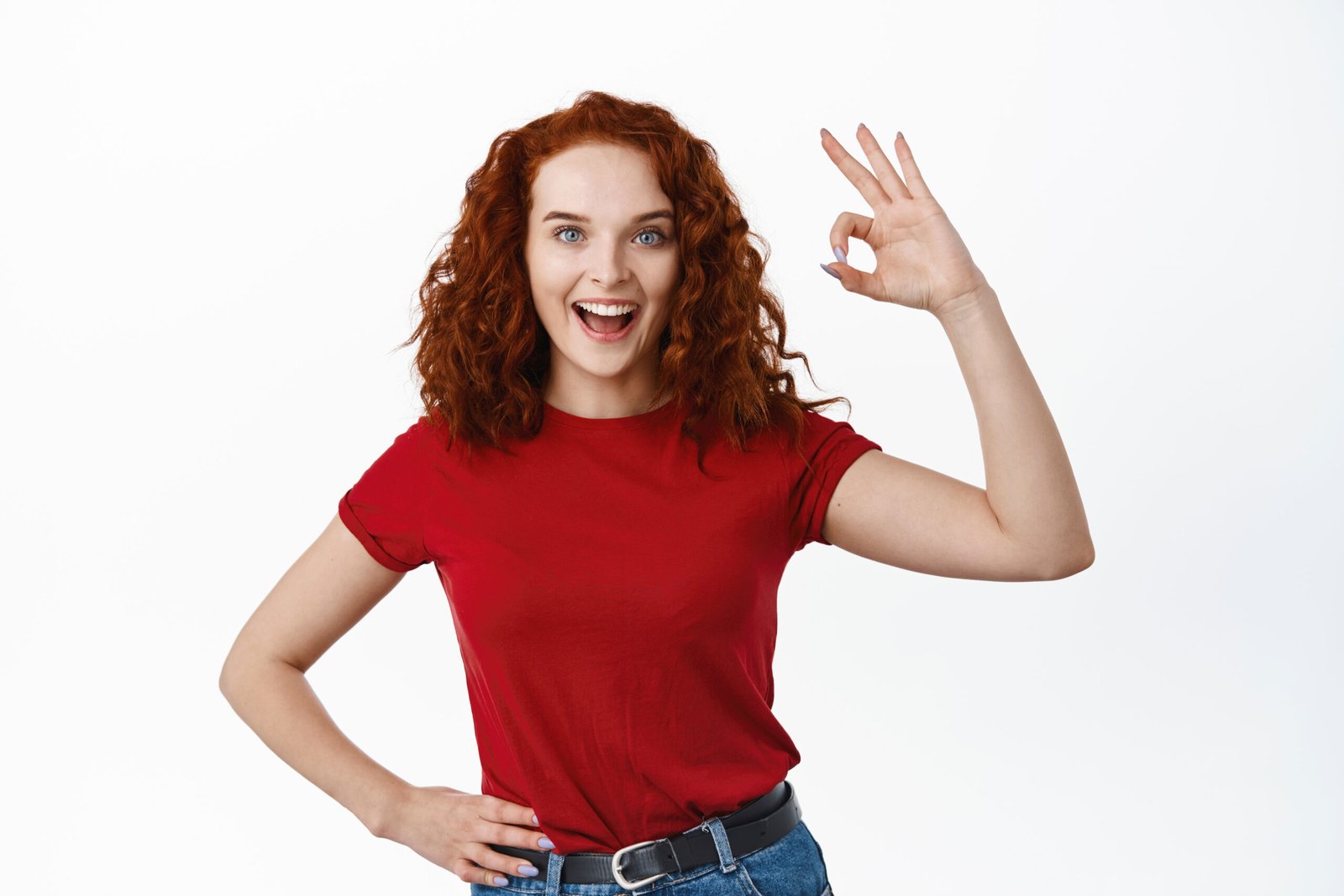 Excellent job. Pleased redhead girl with curly hair say alright yes, showing Okay sign and smiling satisfied, approve good thing, standing over white background